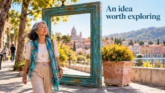An older woman walks beside a freestanding turquoise frame overlooking a town, with the words “An idea worth exploring.”