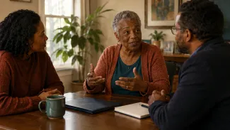 An older Black woman leads a planning conversation at home while her daughter and a trusted professional listen.