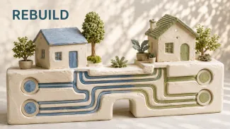 Two ceramic homes stand on a shared foundation with separate blue and green channels beneath the word “REBUILD.”