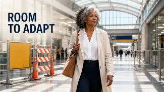 A confident woman walks through a bright concourse past a temporary closure beneath the words “Room to Adapt.”