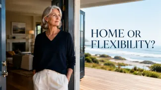A woman approaching retirement stands between her familiar home and an open coastal horizon, considering home equity and financial flexibility after divorce.
