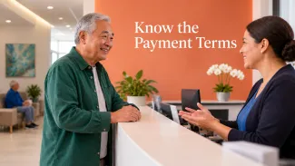 An older man talks with a billing professional at a medical office beneath the words “Know the Payment Terms.”