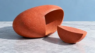 A coral-colored oval sculpture with a section removed and resting beside it on a pale stone surface.