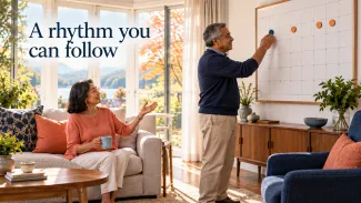 An older couple places markers on a wall calendar in a sunlit living room beneath the words “A rhythm you can follow.”