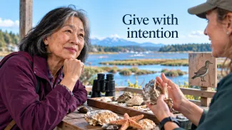 An older woman listens to a coastal conservation volunteer beside a wetland, beneath the words “Give with intention.”