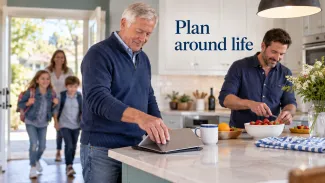 An older man closes his tablet as family gathers in a bright kitchen, beside the words “Plan around life.”