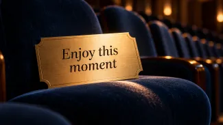 A brass ticket reading “Enjoy this moment” rests on a blue theater seat.