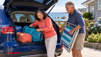 A couple checks how travel bags and a folded beach chair fit in the open cargo area of their familiar car.