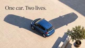 A blue car casts two car-shaped shadows across a sunlit plaza, beneath “One car. Two lives.”