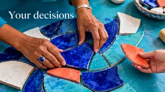 An older woman arranges a blue ceramic mosaic while a friend offers a coral tile; the words “Your decisions” appear above.
