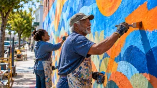 An older father and his adult daughter paint new sections of an already partly completed community mural.