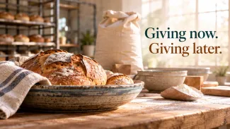 Fresh bread rests beside flour and baking supplies, with the words “Giving now. Giving later.”