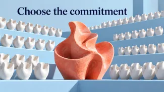 A coral ceramic sculpture stands among rows of white pieces beneath the words “Choose the commitment.”