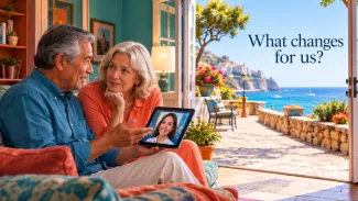 An older couple speaks with an advisor by video beside an open doorway overlooking a coastal promenade, under the words “What changes for us?”