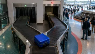 A blue suitcase reaches two diverging airport baggage lanes, representing the receiving-path decision for a pension lump sum.