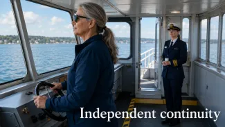A single retiree steers a ferry while a professional relief captain waits behind her, ready for a future handoff.