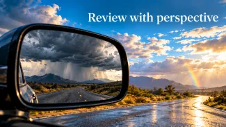 A rear-view mirror reflects storm clouds while the road ahead is sunlit beneath the words “Review with perspective.”
