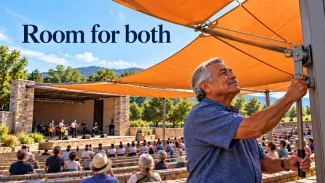 An older man adjusts an orange sunshade at an outdoor community concert beneath the words “Room for both.”