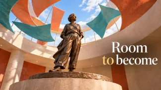 A bronze statue of an older woman stands beneath a coral and teal canopy beside the words “Room to become.”