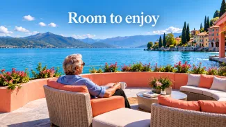 An older couple prepares a colorful salad together on a sunny coastal terrace.