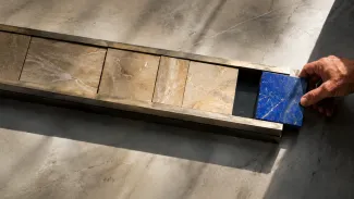 A hand tests a cobalt stone insert against the remaining space in a channel largely filled with pale stone sections.