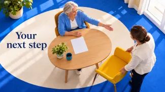 An older woman directs a helper placing a yellow chair beside her table beneath the words “Your next step.”