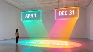 Two illuminated deadline gates marked April 1 and December 31 project overlapping light onto one shared tax year.