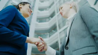 Two businesswomen shaking hands in a modern office building. by Vitaly Gariev courtesy of Unsplash.