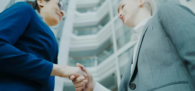 Two businesswomen shaking hands in a modern office building. by Vitaly Gariev courtesy of Unsplash.